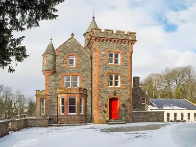 an old brick house with a red door in the snow at Machermore Castle in Newton Stewart