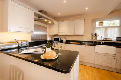 a kitchen with white cabinets and a table with wine glasses at Beck Steps, Elterwater in Chapel Stile