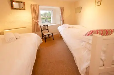 a bedroom with three beds and a chair and a window at End Cottage, Chapel Stile in Chapel Stile