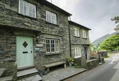 a stone house with a blue door and a bench at Farra Grain, Little Langdale in Little Langdale