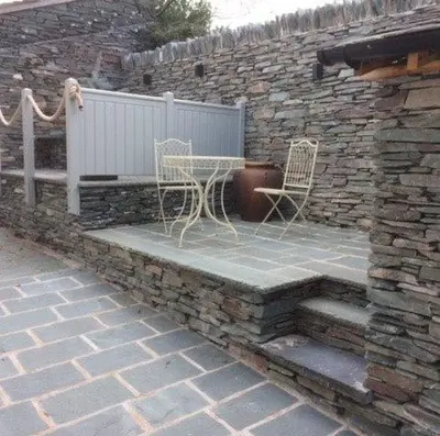 a patio with two chairs and a stone wall at Farra Grain, Little Langdale in Little Langdale