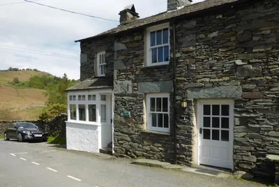 a stone house with white doors and a car parked outside at Nans, Elterwater in Chapel Stile