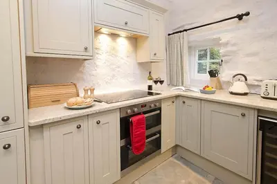 a kitchen with white cabinets and a red towel on the oven at Speddy Cottage, Chapel Stile in Chapel Stile