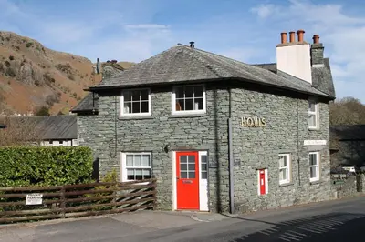 a stone house with a red door on a street at The Old Post Office, Chapel Stile in Chapel Stile