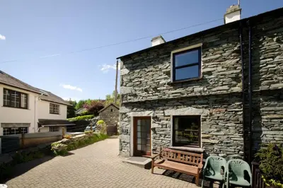 a stone building with a bench and two chairs at Langstrath, Chapel Stile in Chapel Stile