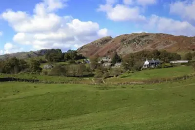 a green field with houses on top of a hill at Lang Parrock, Little Langdale in Little Langdale