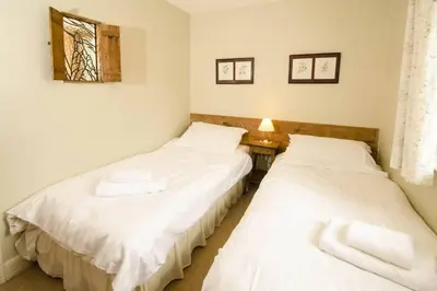 two beds in a room with a table and a window at Juniper Grasmere - Juniper Cottage, Grasmere in Grasmere