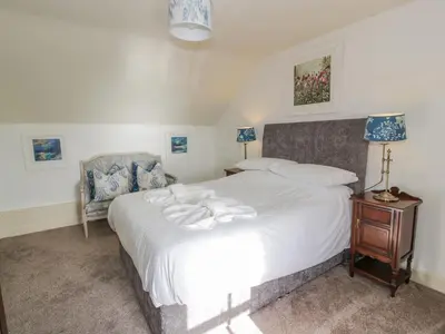a bedroom with a large white bed and a chair at Port Donnel Cottage in Dalbeattie
