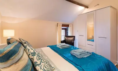 a bedroom with a bed with blue sheets and a chair at Nest Barn in Keswick