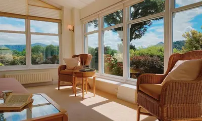 a living room with two chairs and a table and windows at One The Howe in Portinscale
