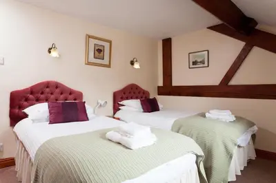 two beds in a hotel room with red chairs at Low Croft Cottage in Grasmere