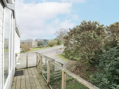 a balcony with a wooden railing next to a house at Oyster Bay Lodge in Dalbeattie