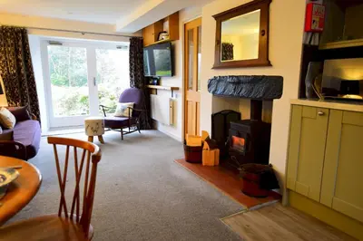 a living room with a fireplace and a couch and a table at Bottom Shop, Elterwater in Chapel Stile