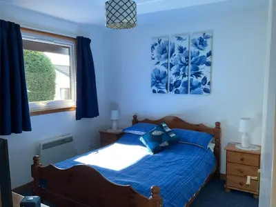 a bedroom with a bed with blue sheets and a window at Heron Lodge, edge of Mabie Forest Dumfries in Dumfries