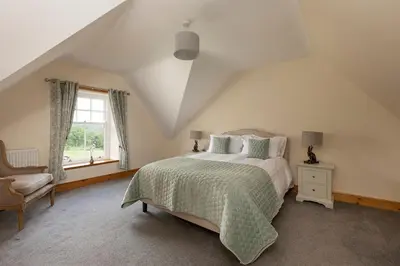 a bedroom with a bed and a chair and a window at Drumlanrig Mains Cottage in Thornhill