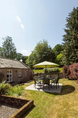 a table and chairs with an umbrella in a yard at Drumlanrig Mains Cottage in Thornhill
