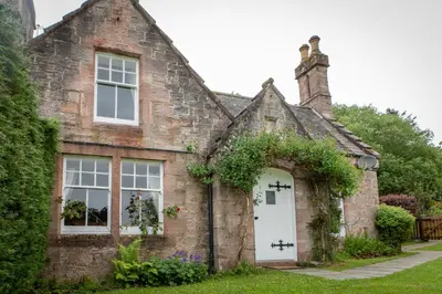 an old brick house with a white door at Drumlanrig Mains Cottage in Thornhill