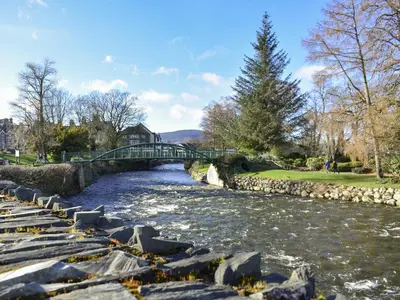 a bridge over a river with rocks in a park at Eskin Den in Keswick