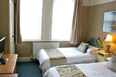 a hotel room with two beds and a desk at Melrose Guest House in Douglas