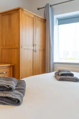 a bedroom with a bed and wooden cabinets and a window at Four Oaks Cottage in Rockcliffe