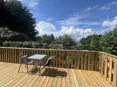 a table and two chairs on a wooden deck at Holly Blue - Cosy wooden lodge Kippford in Dalbeattie