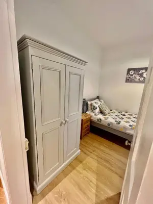 a small bedroom with a white cabinet and a bed at The Blue Door in Kirkcudbright