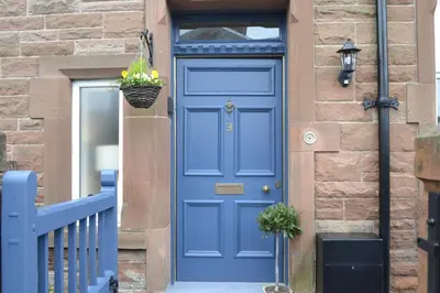 a blue door on a brick building with a basket of flowers at Stunning Period Townhouse with Garden, Walking Distance to Town in Dumfries
