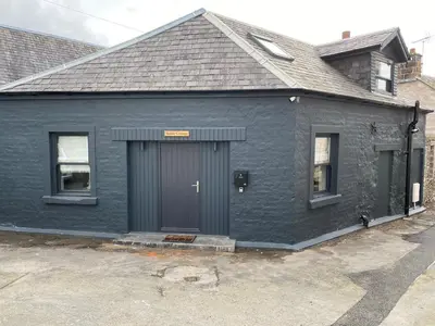 a black house with a gray door and two windows at holidayhomemoffat,com (Stable Cottage) in Moffat