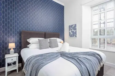 a bedroom with a bed with a blue accent wall at Main Street View - Donnini Apartments in Prestwick