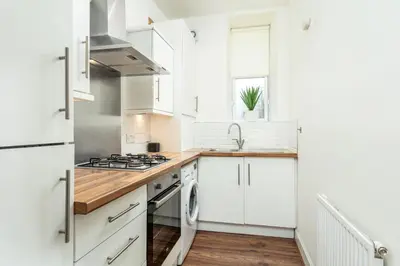 a white kitchen with white cabinets and a sink at Main Street View - Donnini Apartments in Prestwick