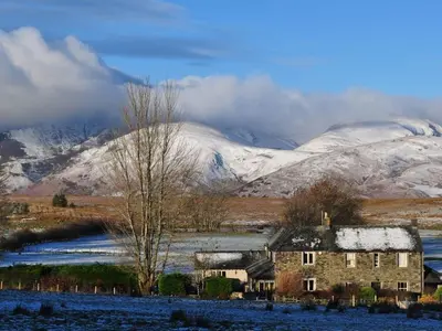 an old house in a field with snow covered mountains at Beckwood in Penrith