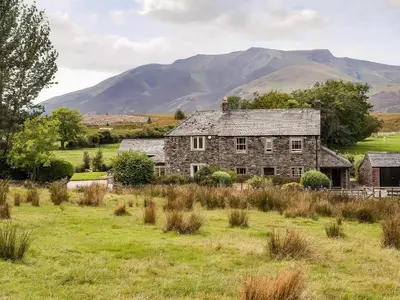 an old stone house in a field with mountains in the background at Beckwood in Penrith