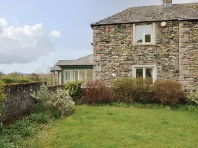 an old stone house with a green yard at Glen Cottage in Penrith