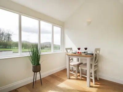 a dining room with a table and chairs and windows at Glen Cottage in Penrith
