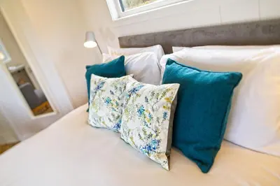 a white bed with blue pillows on it at The Pond Lodges Barstobrick in Ringford