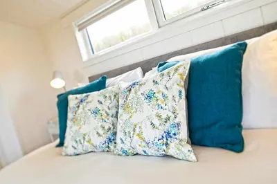 a bed with blue and white pillows and a window at The Pond Lodges Barstobrick in Ringford