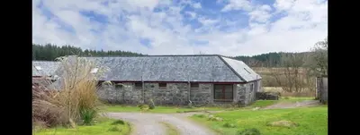 an old stone barn with a dirt road in front of it at Ochiltree cottage in Newton Stewart