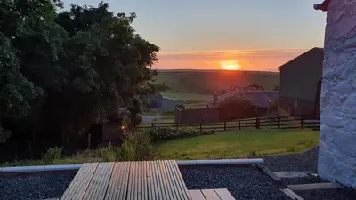 a sunset over a farm with a bench and a barn at Dairy Cottage with sea views in Girvan