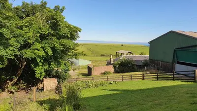 a farm with a fence and a barn and a field at Dairy Cottage with sea views in Girvan