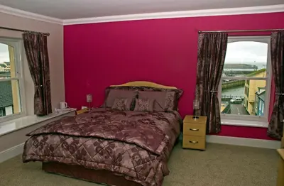 a bedroom with pink walls and a bed and windows at The Golden Lion Hotel in Maryport