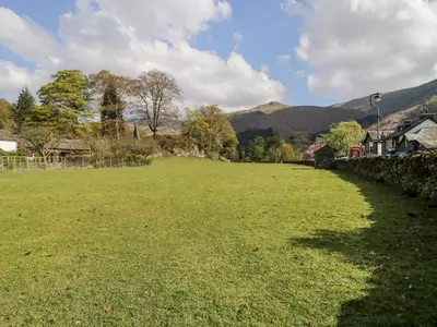 a large grass field with houses and mountains in the background at The Bakers Loft in Ambleside