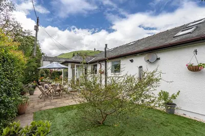 a white house with a patio with chairs and an umbrella at Finest Retreats - The Duck House in Braithwaite