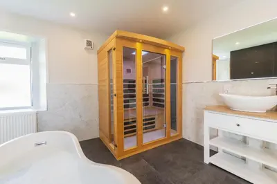 a bathroom with a wooden cabinet and a sink at Nether Newton - Sleeps 12, Hottub, Sauna, Private Garden in Newmilns