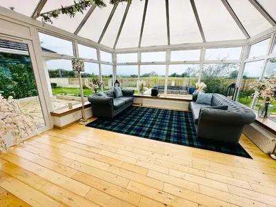 a conservatory with two couches in a room with windows at Alton Villa, Sleeps 12, Great for Families, Undercover Hotub & Games Room in Newmilns