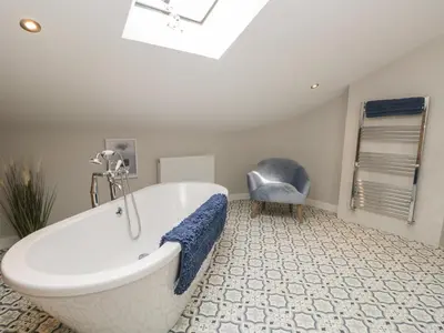 a bathroom with a bath tub and a chair at Carrock Cottage in Dalston