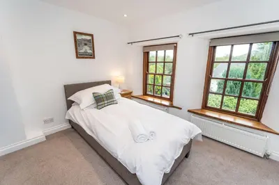 a bedroom with a bed with white sheets and windows at Barf Cottage in Portinscale