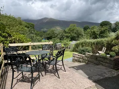a table and chairs on a patio with mountains in the background at Roslin in Portinscale