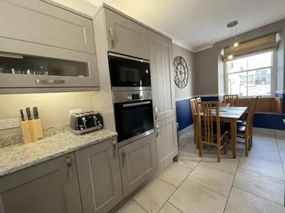 a kitchen with white cabinets and a dining room with a table at Bridge Cottage in Keswick