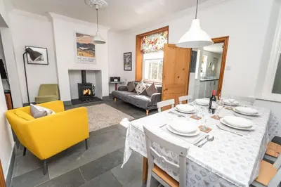 a dining room and living room with a table and yellow chairs at Coleridge Cottage in Keswick