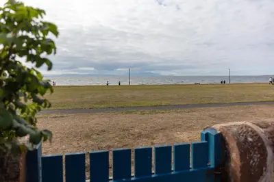 a blue fence in front of a beach at Shore View - Donnini Apartments in Prestwick